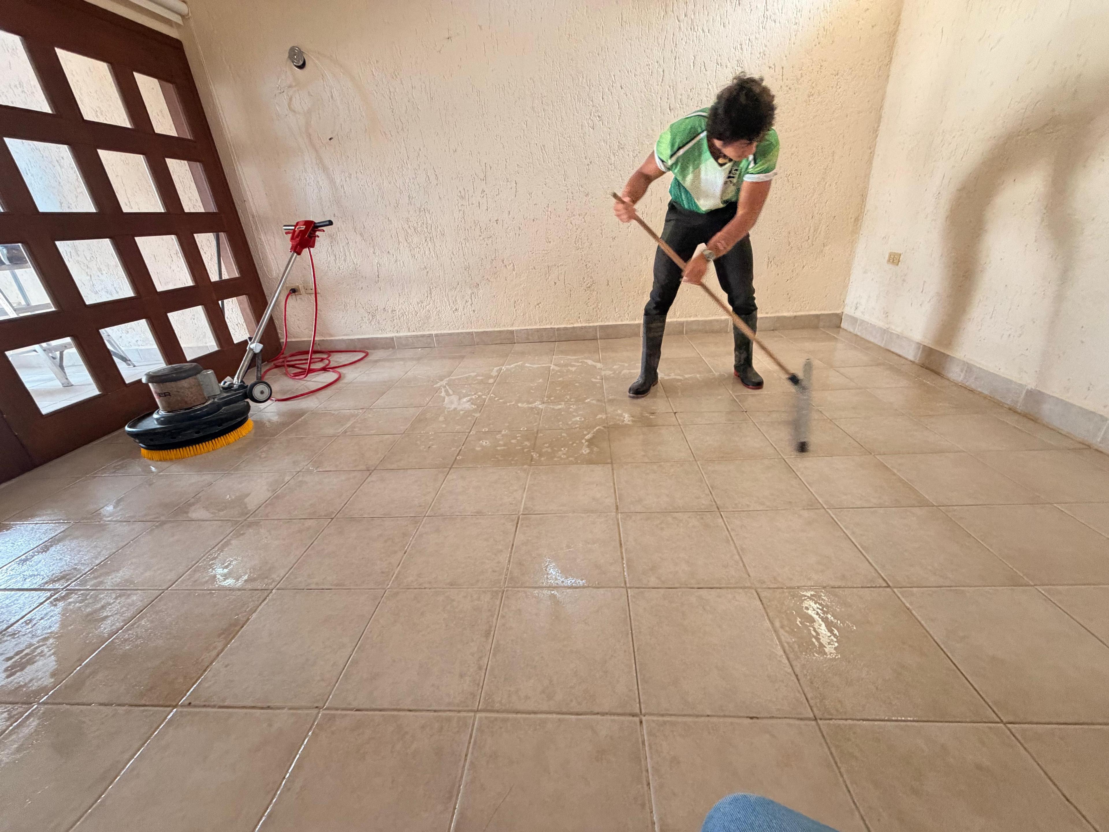Persona fregando un piso de azulejos con un cepillo grande en una habitación.