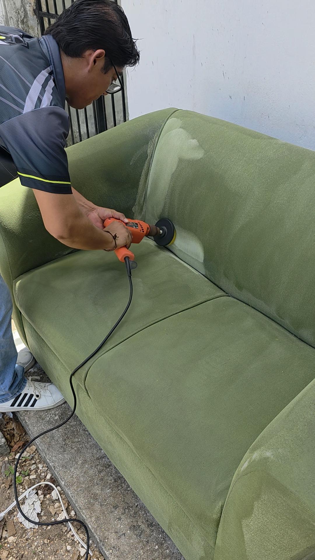Persona usando una herramienta eléctrica para limpiar un sofá verde al aire libre.